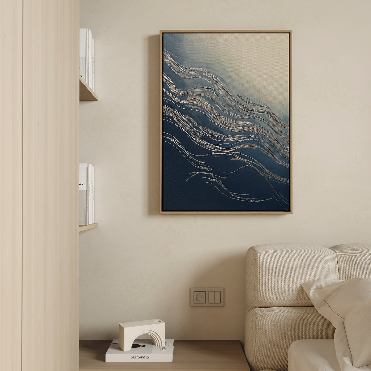 A modern living room wall exudes sophistication, displaying the Silver Current Canvas Art - Vertical with blue and beige wave patterns in a wooden frame. Part of a beige sofa and a light wood shelf with books are also visible.