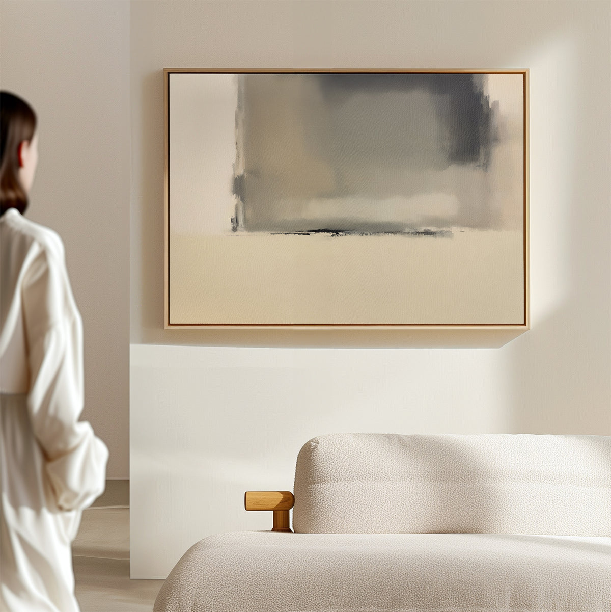 A person stands in a serene, minimalist room with a light-colored sofa and the Smoke Boundary Canvas Art - Horizontal, a striking abstract piece in soft neutral tones, displayed on the wall.