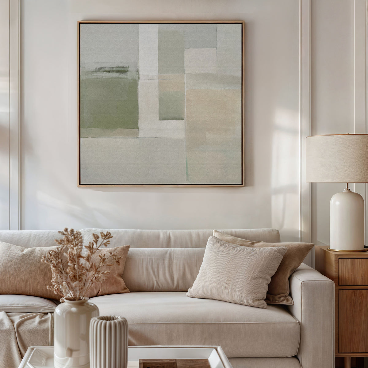 A modern living room featuring a beige sofa, neutral cushions, a wooden side table with a ceramic lamp, dried flowers in a vase, and the Soft Geometric Planes Canvas Art - Square on the wall as sunlight streams in.