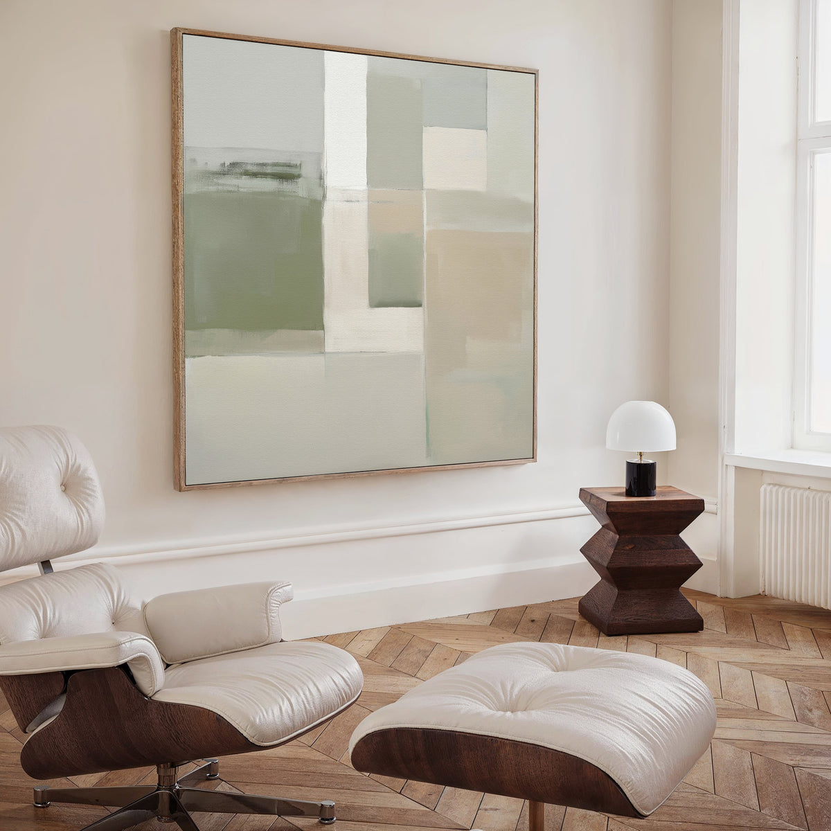A modern, minimalist living space featuring a white leather lounge chair and ottoman, a small wooden side table with a round white lamp, and the Soft Geometric Planes Canvas Art - Square that enhances the contemporary vibe.