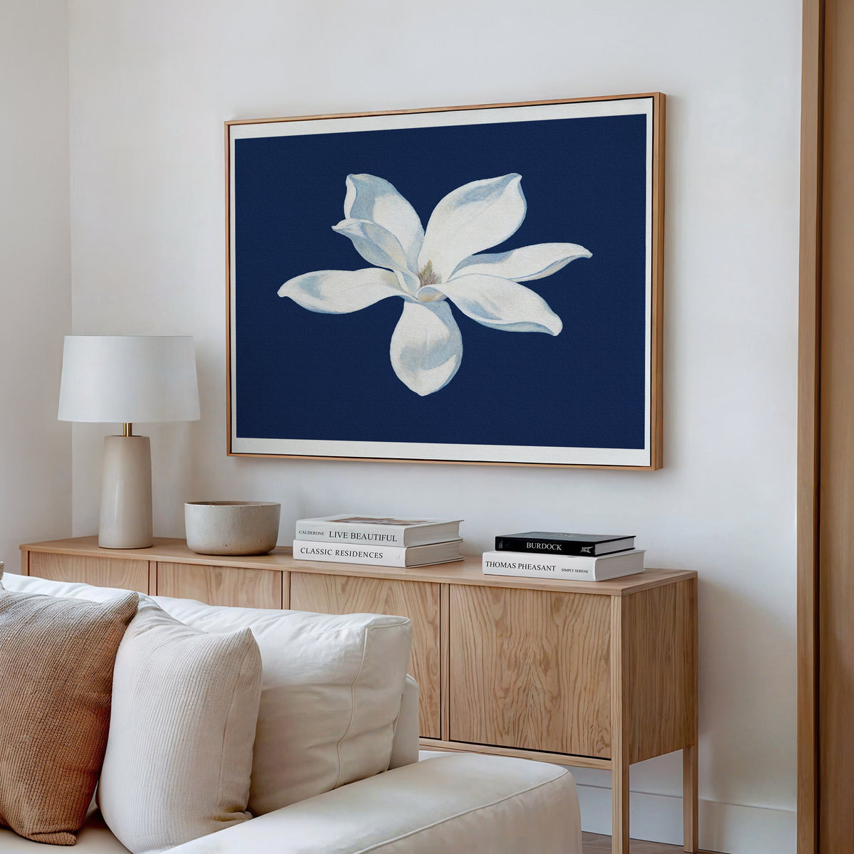 A modern living room showcases neutral décor and a light wood sideboard topped with books and a lamp, while the Starlit Magnolia Canvas Art - Horizontal serves as striking contemporary wall art above.