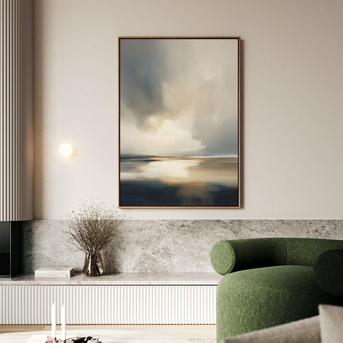 A modern living room features a green curved sofa, marble bench, and neutral walls. The Stormy Tides Canvas Art - Vertical in soft blue, gray, and beige tones adds a serene touch to this Nordic Park-inspired space with a minimalist vase of dried branches.