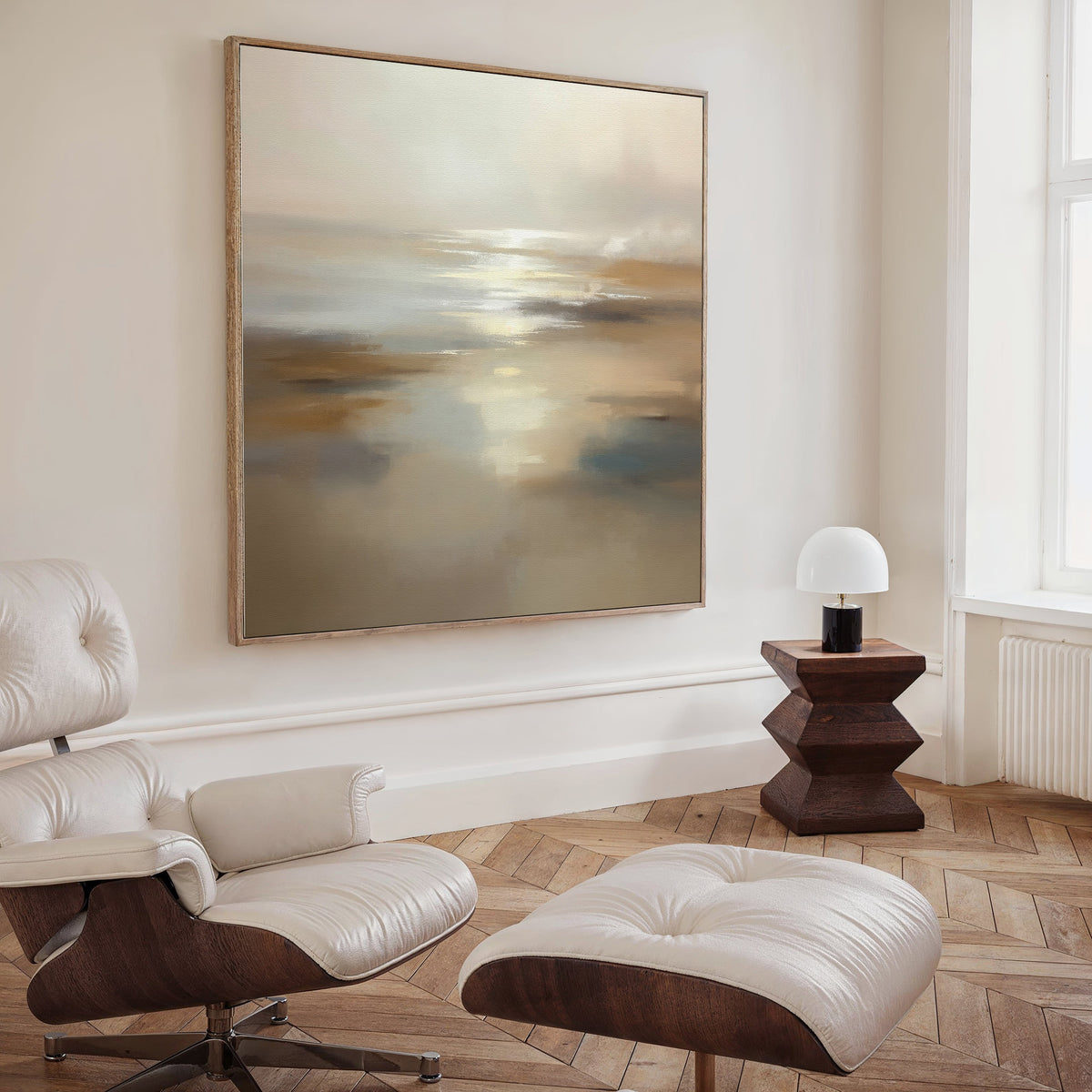 A minimal living room features the Sunlit Waters Canvas Art - Square as a striking focal point, paired with a white leather lounge chair and ottoman, a geometric dark wood side table, and a small white lamp on herringbone wood flooring.