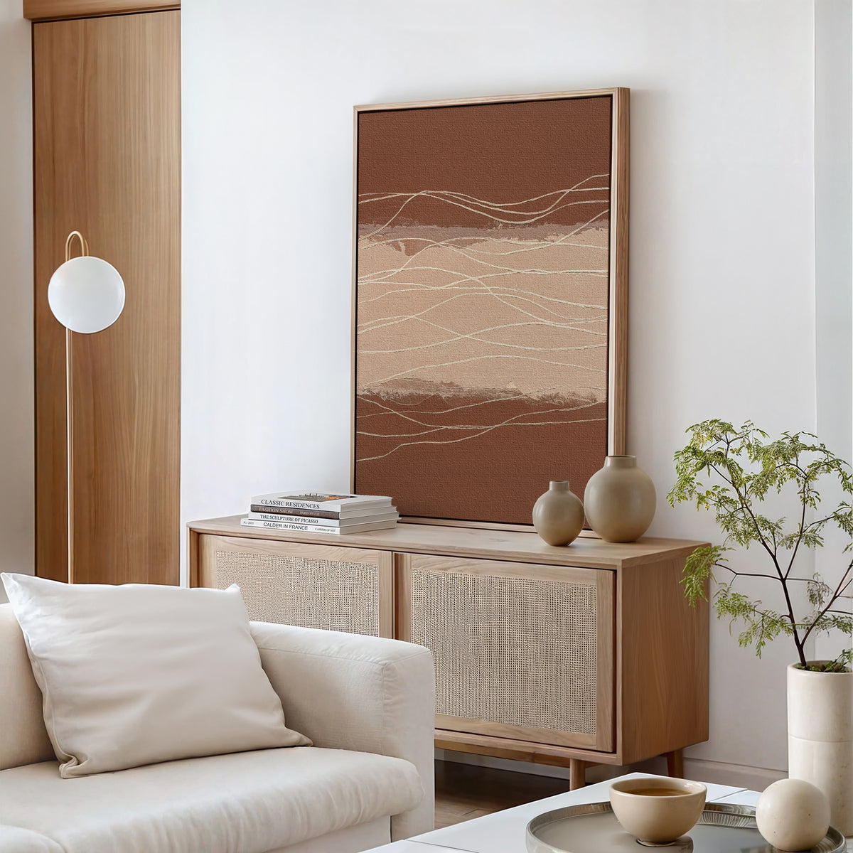 Minimalist living room with light wood furniture, a beige sofa with a white pillow, a sideboard with vases and books, Terracotta Currents Canvas Art - Vertical in earth tones on the wall, a round pendant light, and a potted plant on the coffee table.