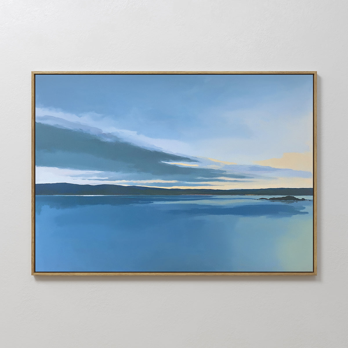 The Tranquil Reflections Canvas Art - Horizontal, featuring a serene blue lake with distant landforms and gentle yellow hues, is ideal as peaceful wall art or calming bedroom decor, displayed here on a plain white wall.