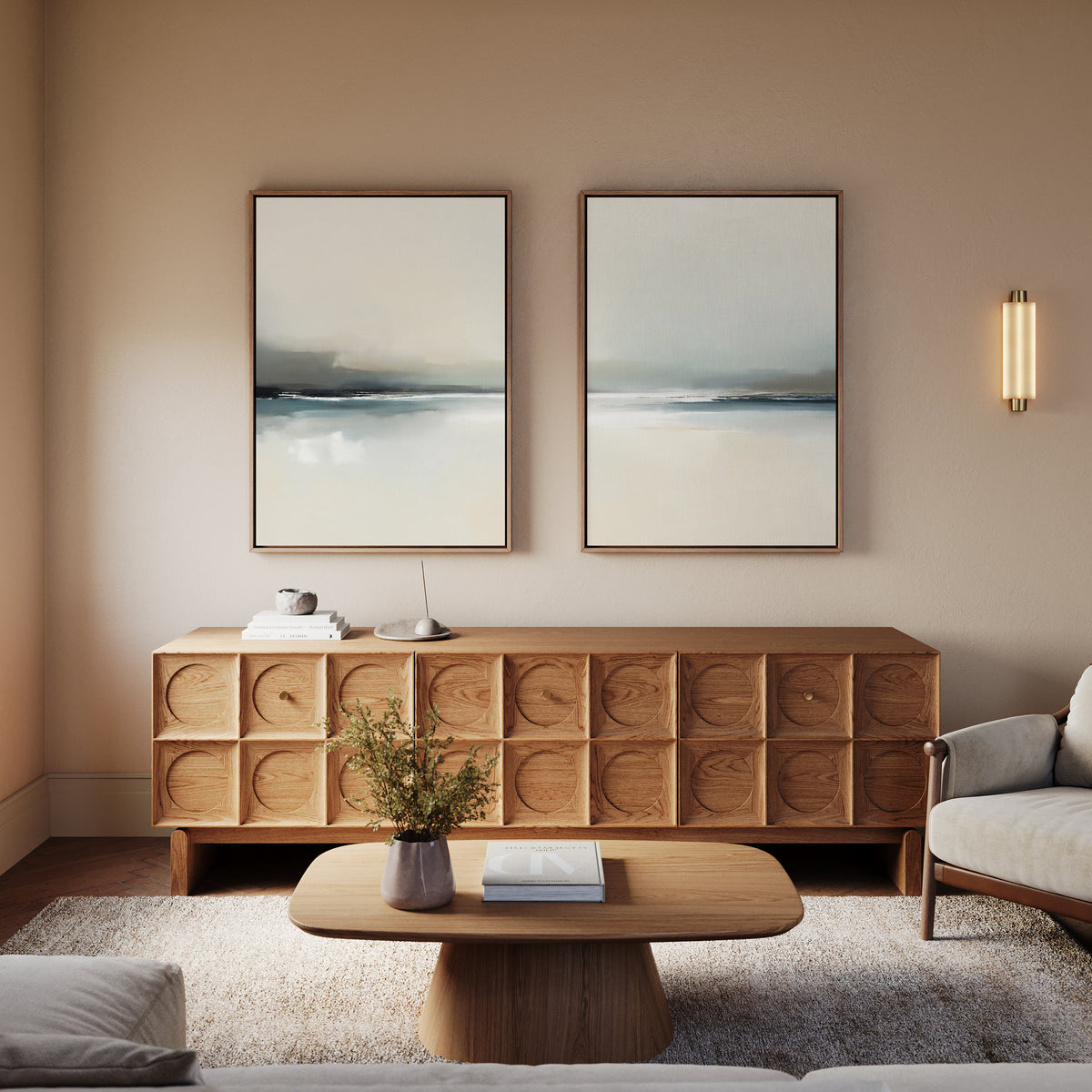 A modern living room with a wooden cabinet, coffee table, neutral armchair, Veiled Estuary - Set Of 2 wall art, a small plant, soft lighting, and minimalist decor.