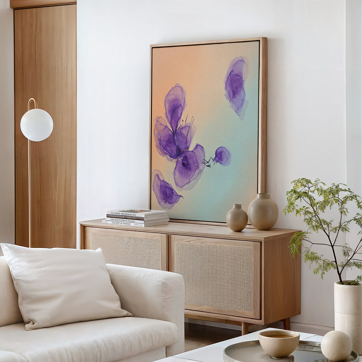 A modern living room features a light wood sideboard, Nordic Park-inspired decor, the Violet Dreams Canvas Art – Vertical, neutral vases, a stack of books, a small plant, white sofa, and minimalist accents in soft natural tones.