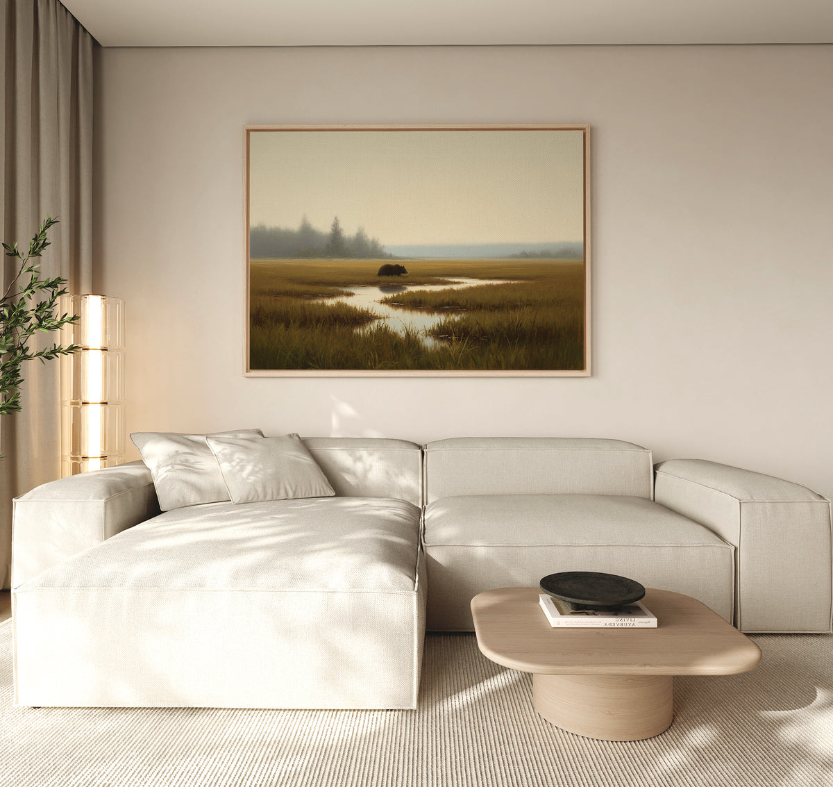 A modern living room featuring a light beige sectional sofa, wooden coffee table with a black bowl, tall plant, and the Wetland Bear Canvas Art - Horizontal depicting serene river and fields. Neutral tones and natural light create a tranquil atmosphere.