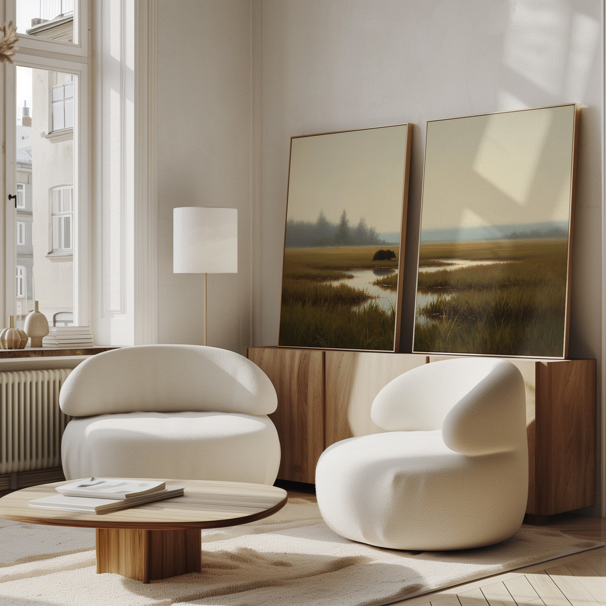 Two modern white rounded armchairs and a low wooden table sit in a bright living room with large windows. On the wooden sideboard are two framed "Wetland Bear - Set Of 2" art pieces against the wall.