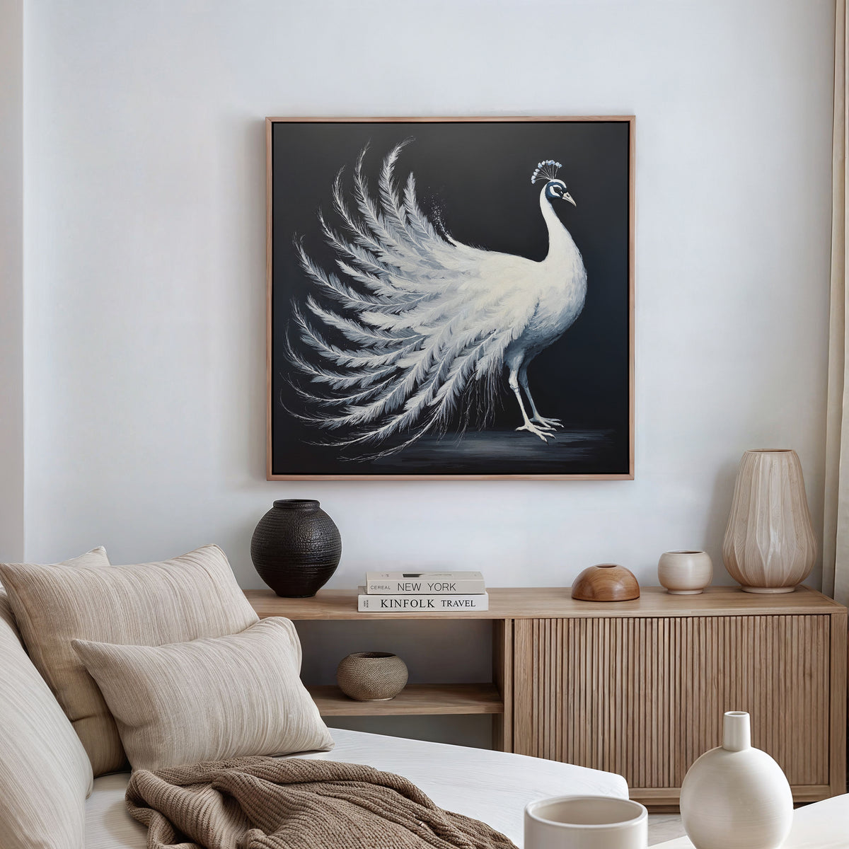 A modern living room with a beige sofa and wooden sideboard, accented by neutral cushions and ceramics. The White Peacock Display Canvas Art - Square hangs as a striking focal point on the wall.