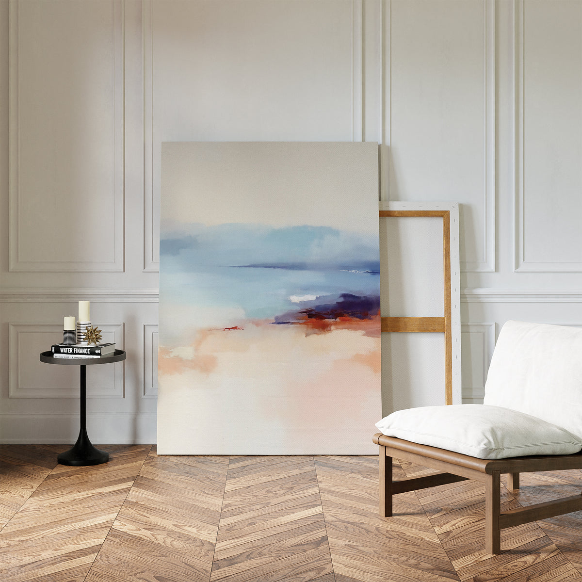 The Windswept Coastline Canvas Art - Vertical, featuring soft pastel blue, peach, and purple abstract tones, leans against a white paneled wall near a cushioned wooden chair and black side table on a herringbone wood floor.