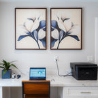 A modern home office setup with a laptop and supplies on a white marble desk features the Navy Magnolia Set of 2 as striking floral wall art above the workspace, adding elegant and modern decor to the scene.