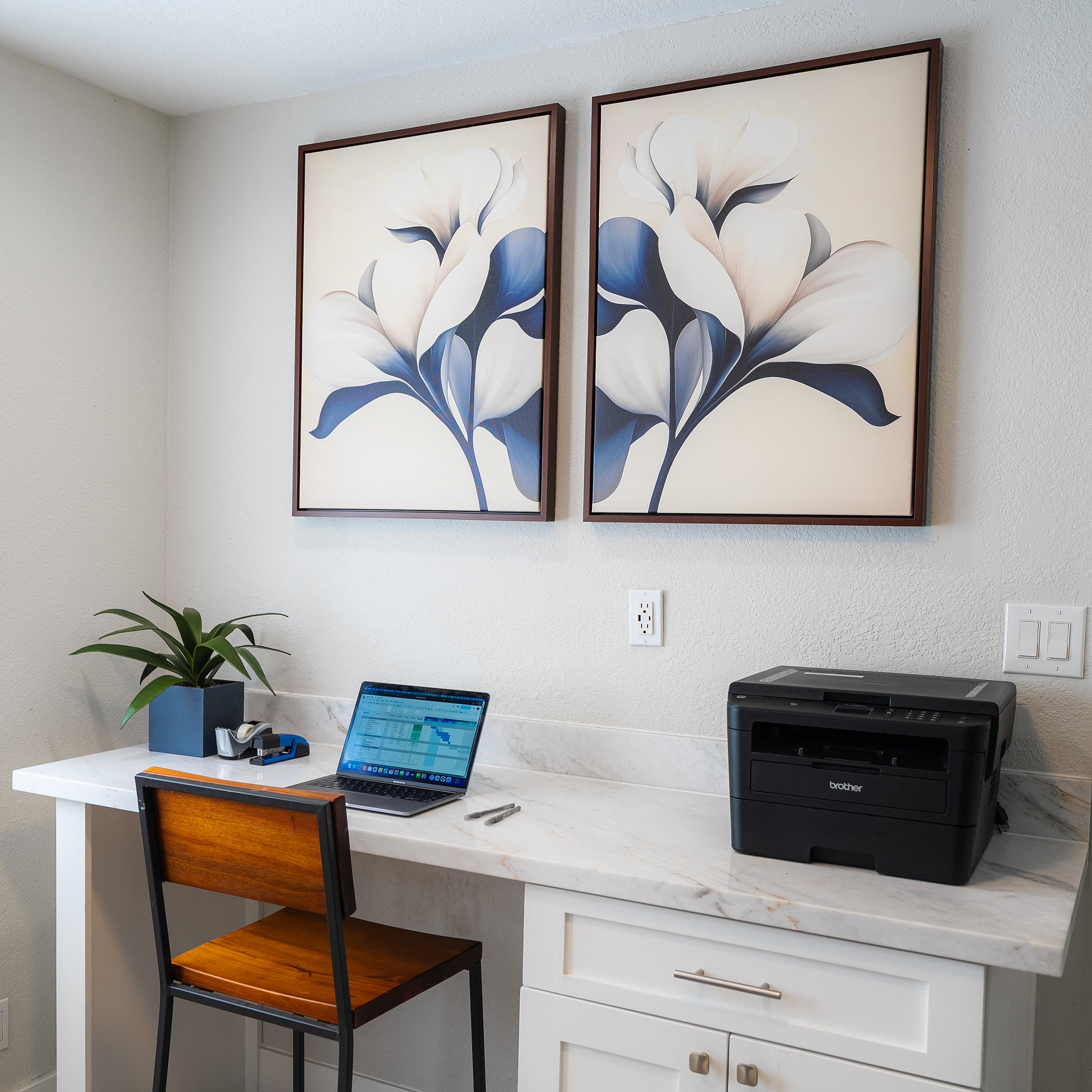 A modern home office setup with a marble desk, wooden chair, laptop, printer, plant, and the Navy Magnolia Set of 2 prints as striking modern wall decor above the workspace.