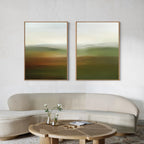 A modern living room features a curved beige sofa, a round wooden coffee table with a vase of white flowers, and the Lush Landscape Set of 2 abstract wall art prints in earthy tones displayed on a light-colored wall.