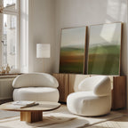 A modern living room with curved white armchairs, a low wooden coffee table, and soft natural light streaming through large windows, featuring the Lush Landscape Set of 2 wall art prints for elegant decor.
