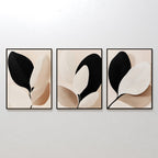The Monochrome Flora Set of 3 features framed abstract art prints with minimalist leaf designs in black, beige, and white—perfect botanical wall art for modern living rooms, displayed together on a light-toned wall.