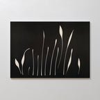 Botanical Silhouettes Abstract Canvas Art showcases elongated white floral and grass shapes on a solid black background, displayed on a plain white wall.