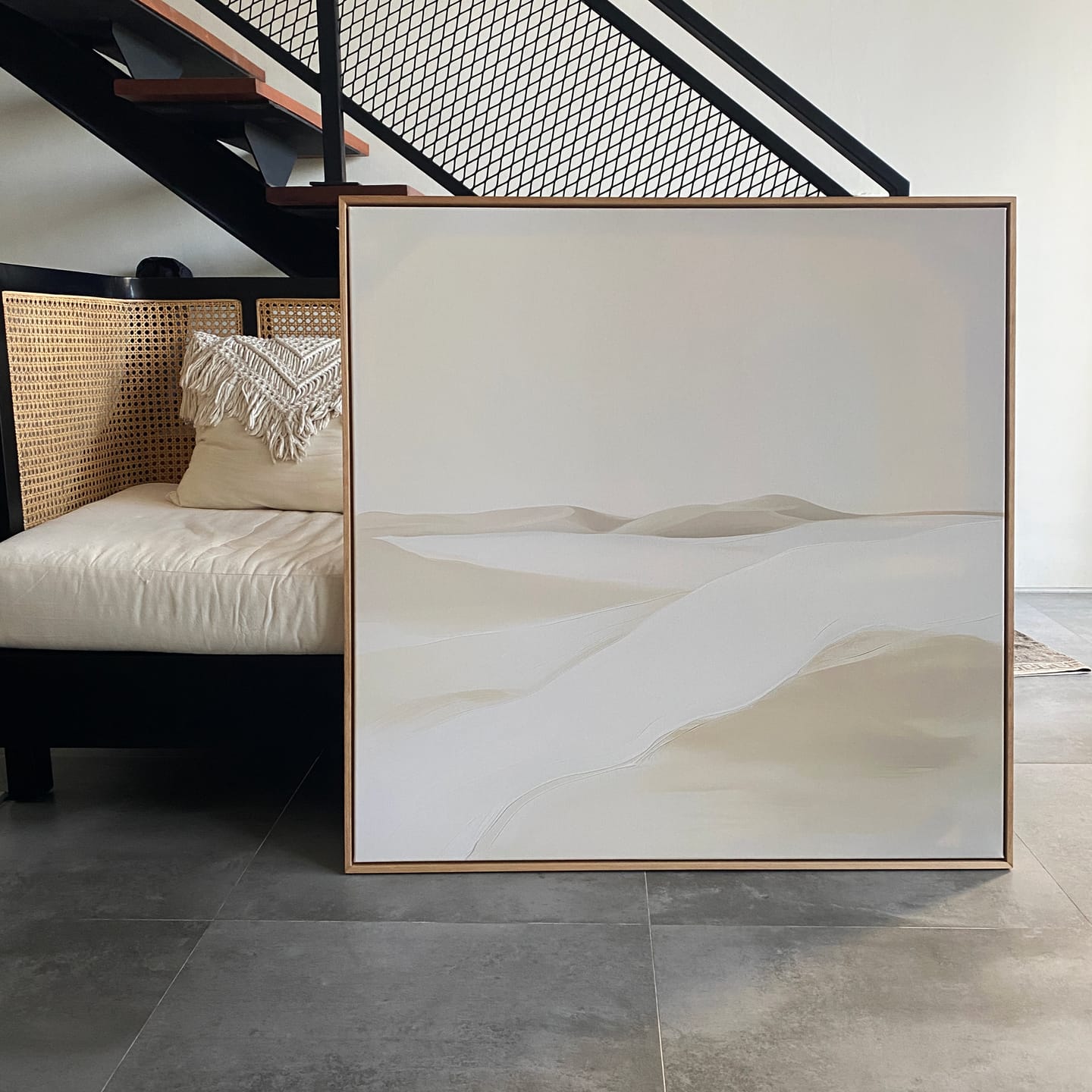 Misty Vale Abstract Canvas Art features soft, pale sand dunes in neutral tones. Displayed on a tiled floor, leaning against a creamy cushioned bench beneath a modern staircase—perfect minimalist wall art for living room decor.