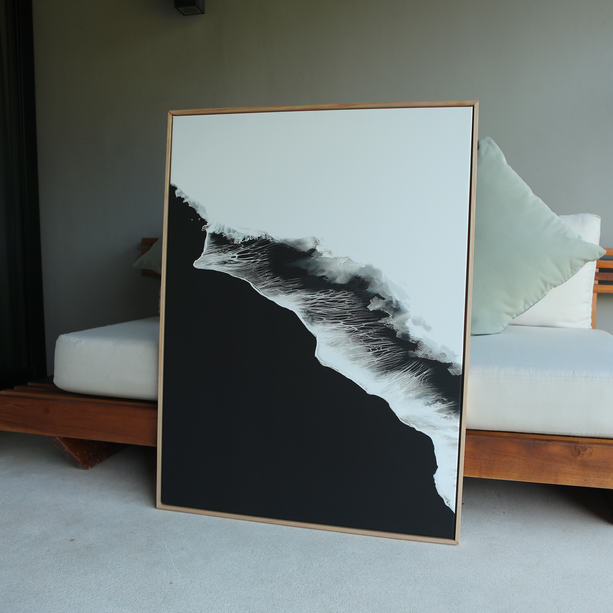 The Black Ocean Abstract Canvas Art, featuring bold black and white contrasts in an abstract wave or mountain design, is framed and leans against a cushioned wooden bench indoors.