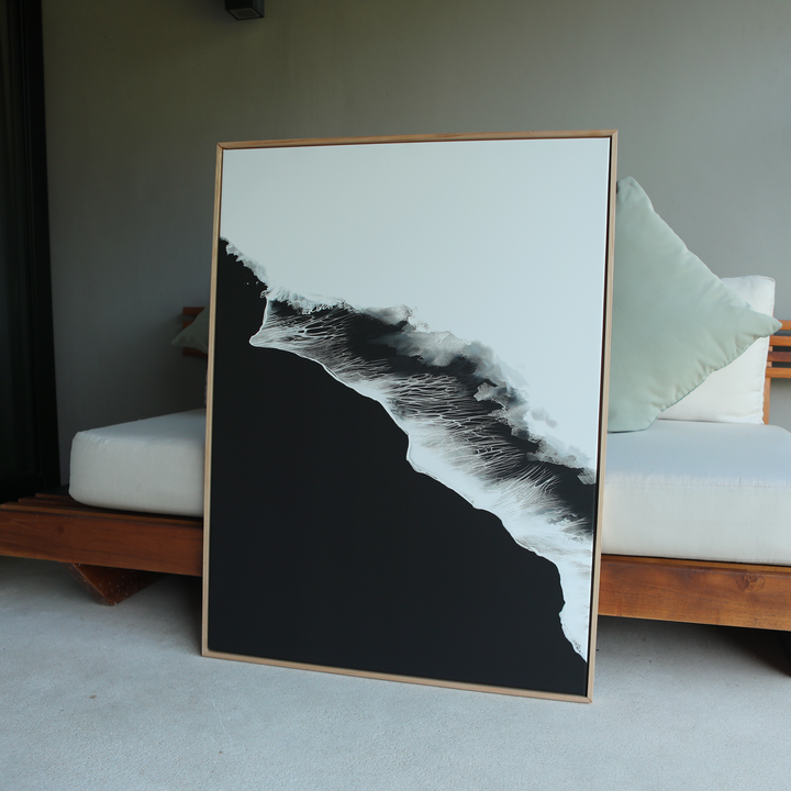 The Black Ocean Abstract Canvas Art, featuring bold black and white contrasts in an abstract wave or mountain design, is framed and leans against a cushioned wooden bench indoors.