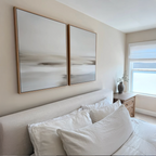 A bright, minimalist bedroom features a beige bed with white bedding, a wooden nightstand, and natural light from a window. Above the headboard hangs the Tranquil Shifts Set of 2 wall art pieces for a modern touch.