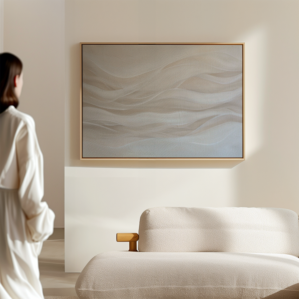 A woman in a white robe stands in a minimal, modern room, looking at the Sandy Hues Abstract Canvas Art with soft wavy lines in neutral tones, displayed above a light-colored, textured sofa.
