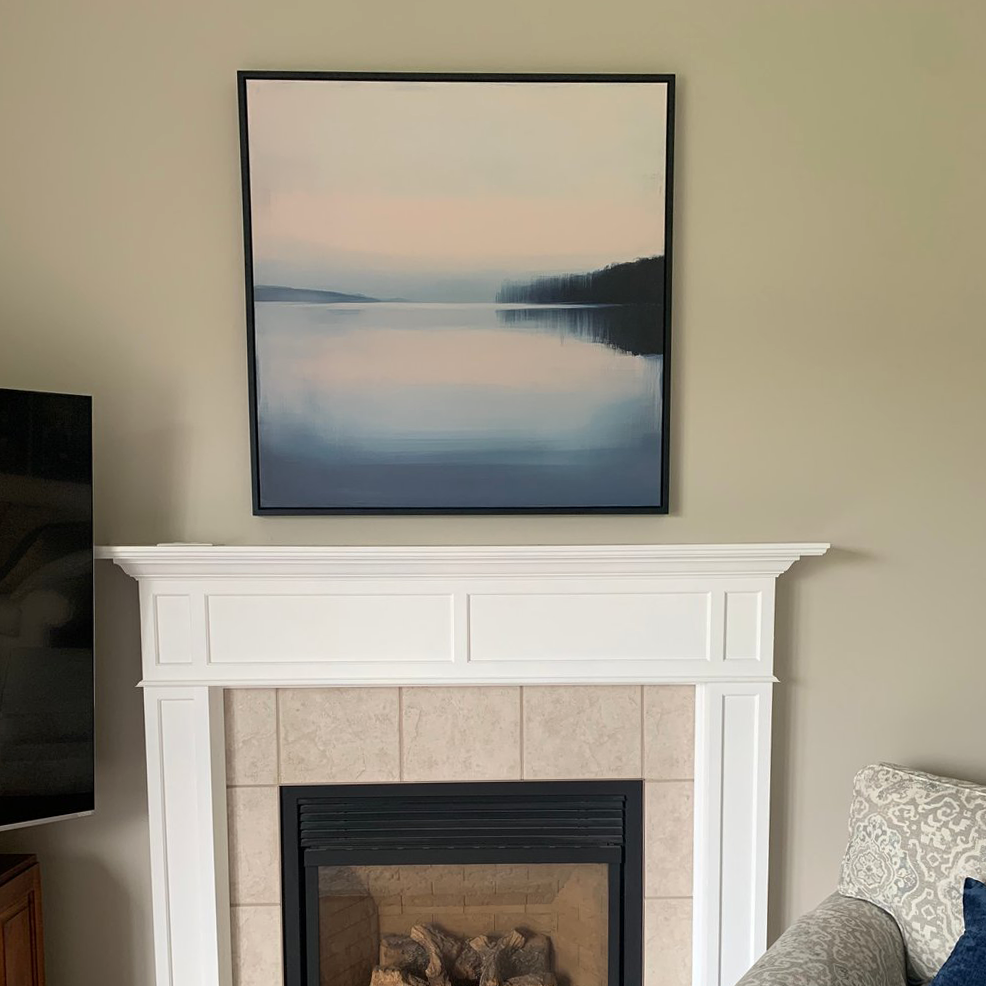 Echo Lake Canvas Art hangs above a white fireplace with beige tiles. The room has neutral walls, part of a TV on the left, and a patterned armchair on the right—perfect as calming bedroom decor.