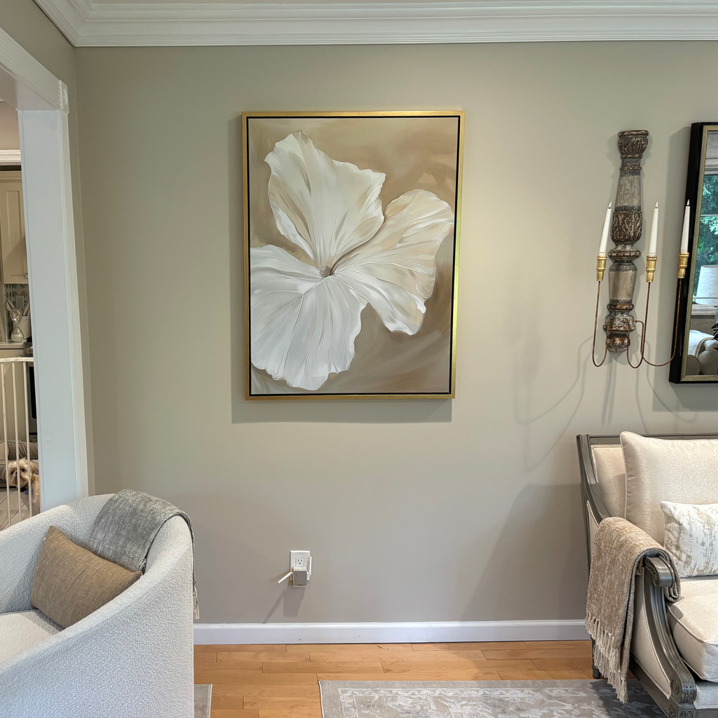 The Aqua Flora Abstract Canvas Art in a gold frame hangs on a beige wall above a power outlet, with a modern armchair and gray sofa nearby, adding cozy and inviting decor to this well-lit living room.