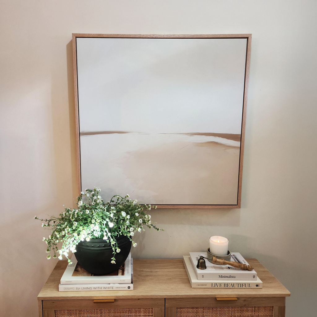 The Serene Expanse Abstract Canvas Art by My Store hangs above a wooden cabinet adorned with stacked books, a black planter of greenery, and a lit candle with matches, creating a calm and serene modern wall art display.