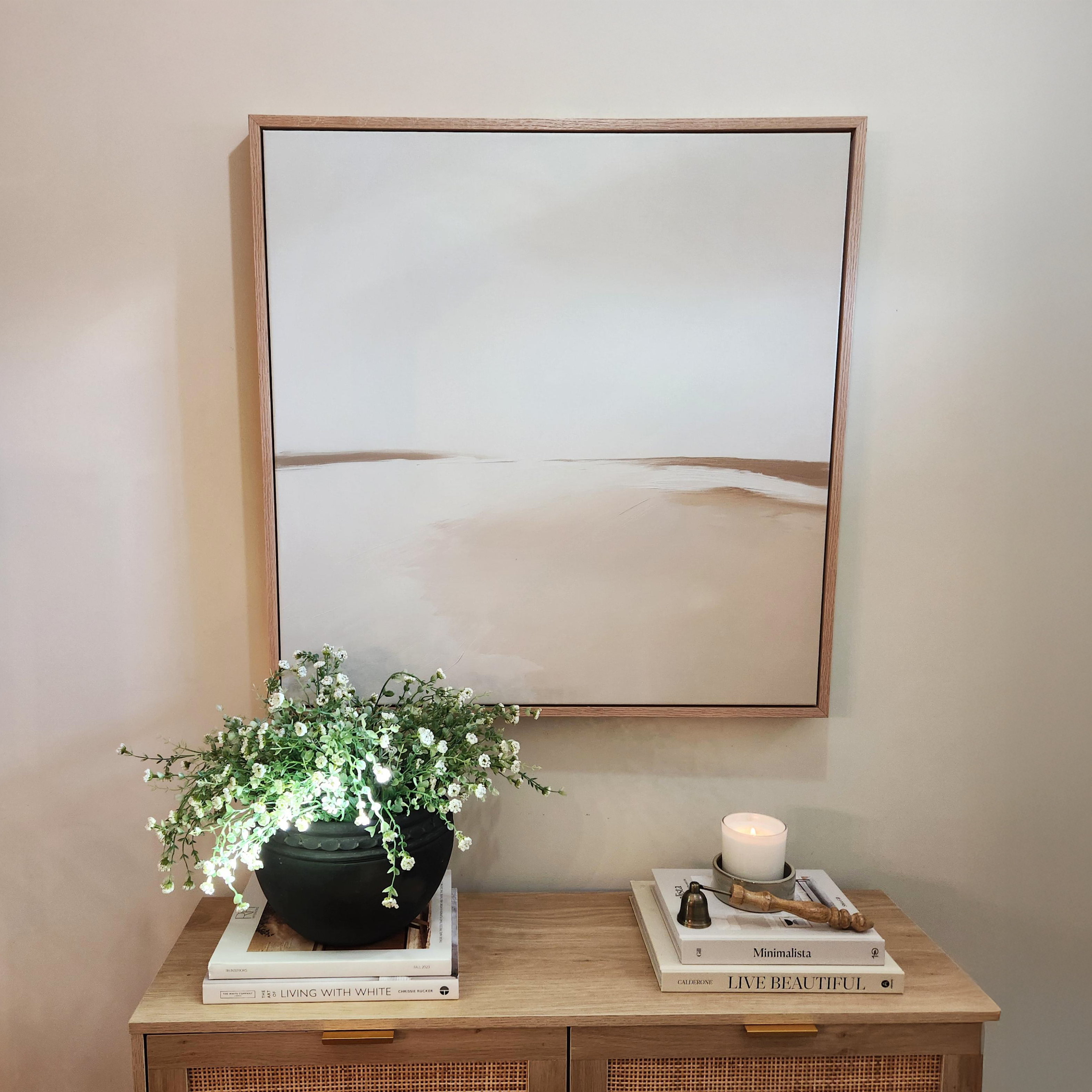 The Serene Expanse Abstract Canvas Art by My Store hangs above a wooden cabinet adorned with stacked books, a black planter of greenery, and a lit candle with matches, creating a calm and serene modern wall art display.
