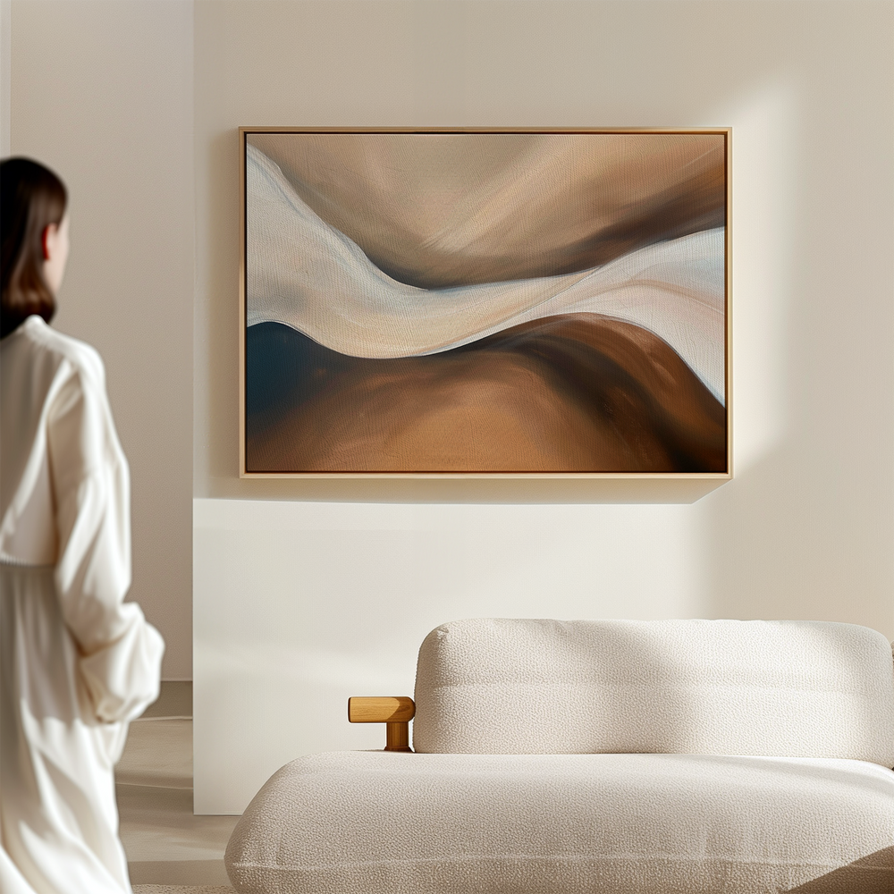 A person in a white robe stands in a modern living room, admiring the Neutral Landscape River Abstract Canvas Art with beige, brown, and white tones hanging above a light sofa as part of the serene decor.