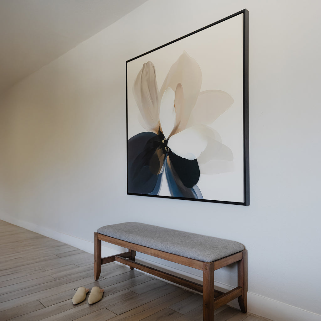 A minimalist hallway showcases a wooden bench with a gray cushion, beige slippers on the floor, and the Whispering Petals Canvas Art—a large, abstract flower painting in soft neutrals—hanging above the bench.