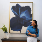 A woman in a blue shirt and white pants stands before the striking Midnight Bloom Abstract Canvas Art, with a small table holding a vase of greenery and a candle adding to the modern wall decor beside her.