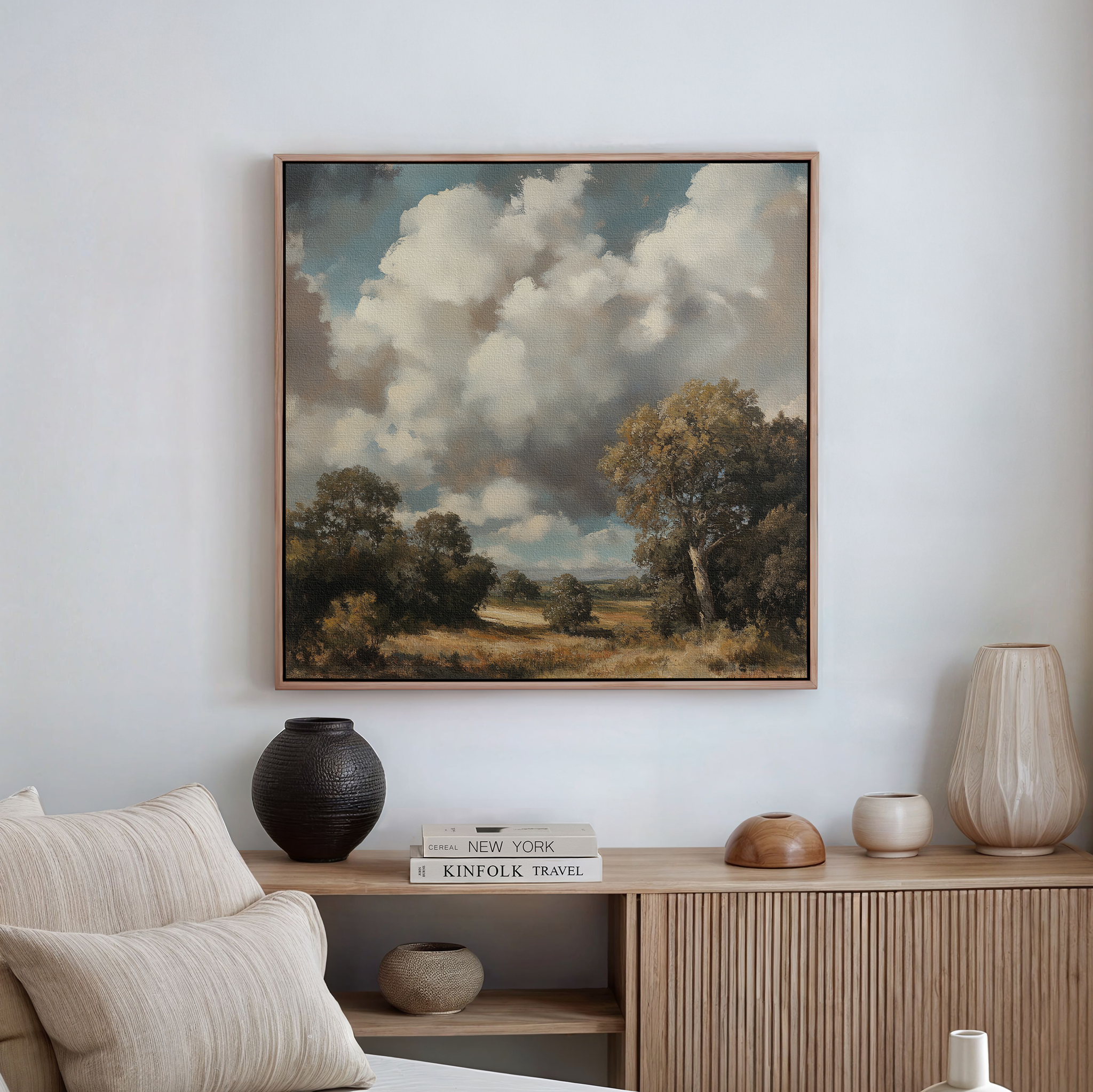 The Gathering Storm Canvas Art, with its depiction of trees and a cloudy sky, hangs above a wooden sideboard adorned with vases, a book, and decor, bringing refined elegance to this minimalist living room in neutral tones.