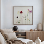 A cozy, modern living room features a light sofa, neutral cushions, wooden sideboard, decorative vases, books, and the Wild Flower Canvas Art—a large painting of red and pink flowers that brightens the white wall.