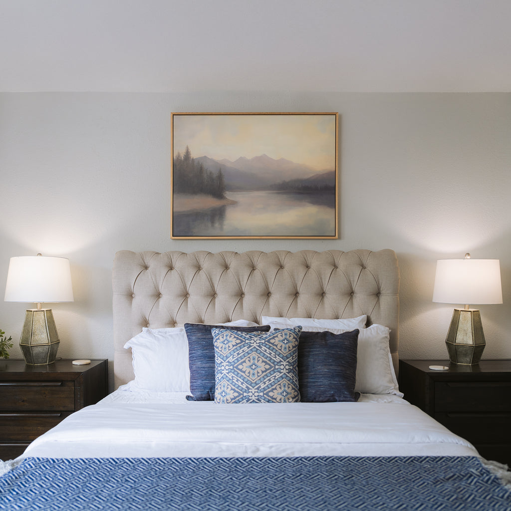 A neatly made bed with blue and white pillows and a blue throw blanket sits between two dark wood nightstands. Above the tufted headboard, Smoky Peaks Canvas Art adds charming mountain wall art to the room.