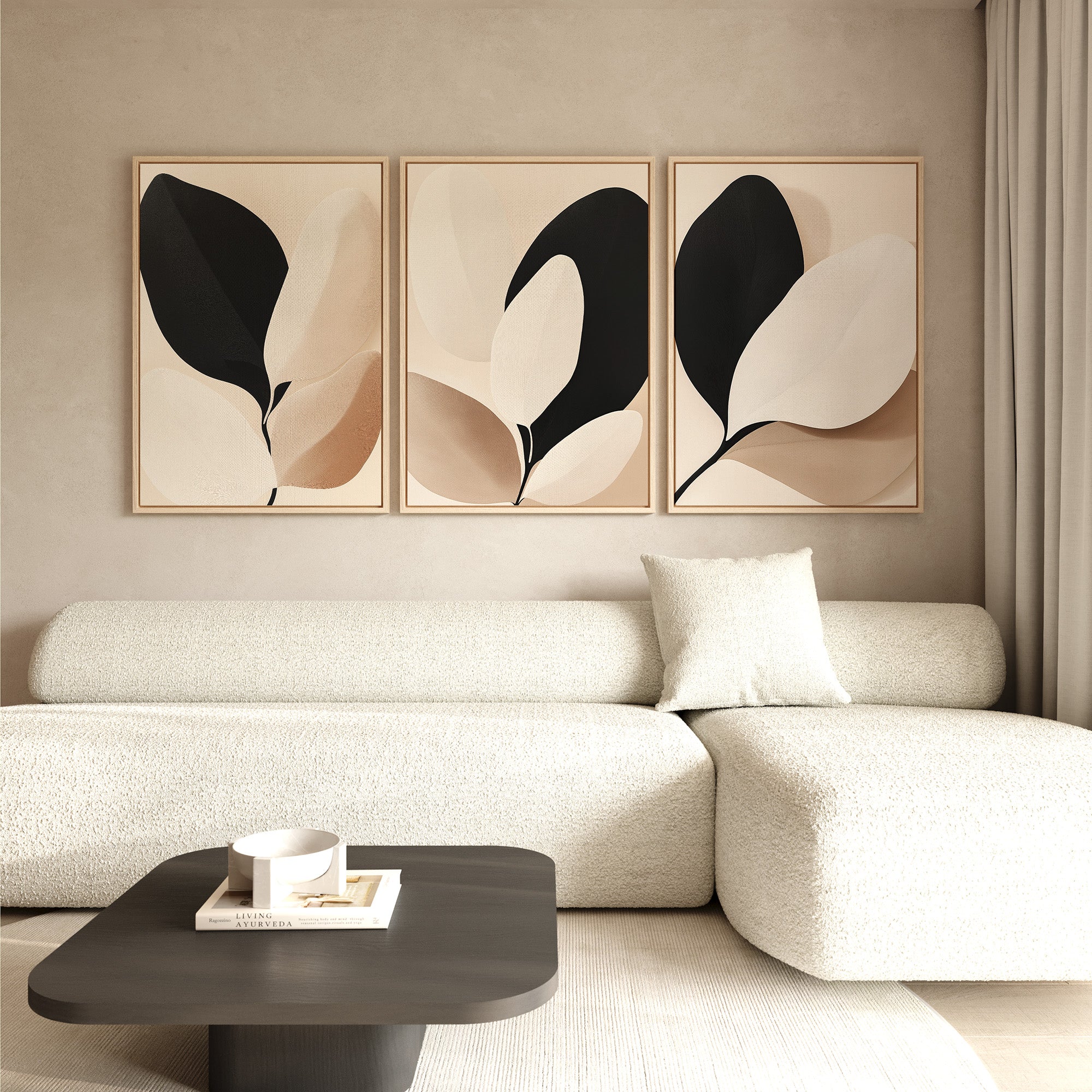 A minimalist living room features a textured white sofa with a cushion, a black coffee table with books, and the Monochrome Flora Set of 3 abstract botanical wall art in neutral tones displayed on a beige wall for modern decor.