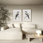 A modern living room features a light beige sectional sofa, a small coffee table with a lamp and books, an indoor plant, and the Still Perch Set of 2 bird art prints above the sofa for added charm.