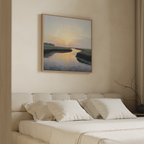 A neutral-toned bedroom features an upholstered bed with white bedding and three pillows. Above the bed hangs the Tidal Whispers Canvas Art - Square, while a branch decorates the minimalist nightstand for a serene ambiance.