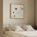 A modern bedroom featuring a beige upholstered headboard, neatly made bed with white bedding, and the elegant Wild Flower Canvas Art displaying red, pink, and purple flowers above the bed.