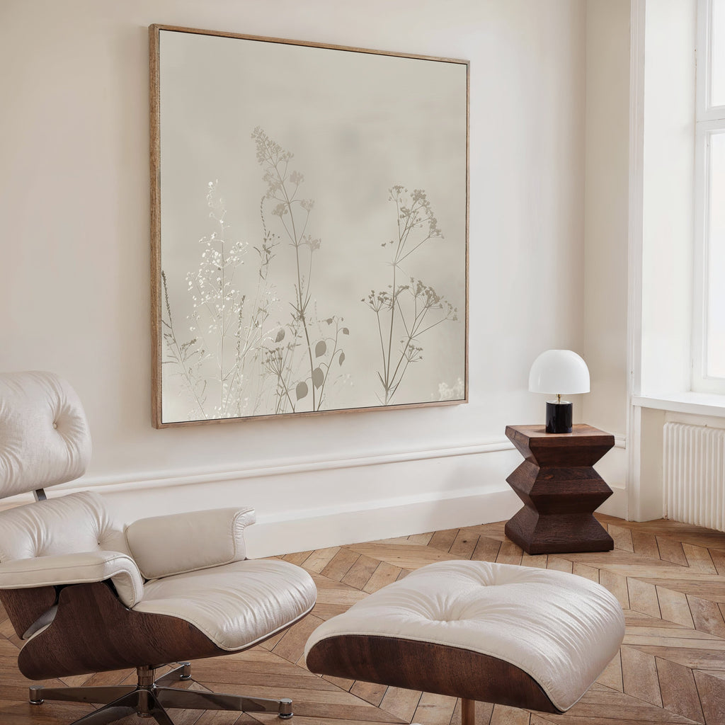 A minimalist living room featuring a cream lounge chair and ottoman, dark wood side table with modern white lamp, herringbone wood floor, and the Floral Symphony Abstract Canvas Art above the chair—perfect for stylish decor.