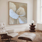 A modern living room featuring a cream leather lounge chair and ottoman, a geometric dark wood side table with a white lamp, and the Floral Whisper Abstract Canvas Art in neutral tones as striking wall décor.