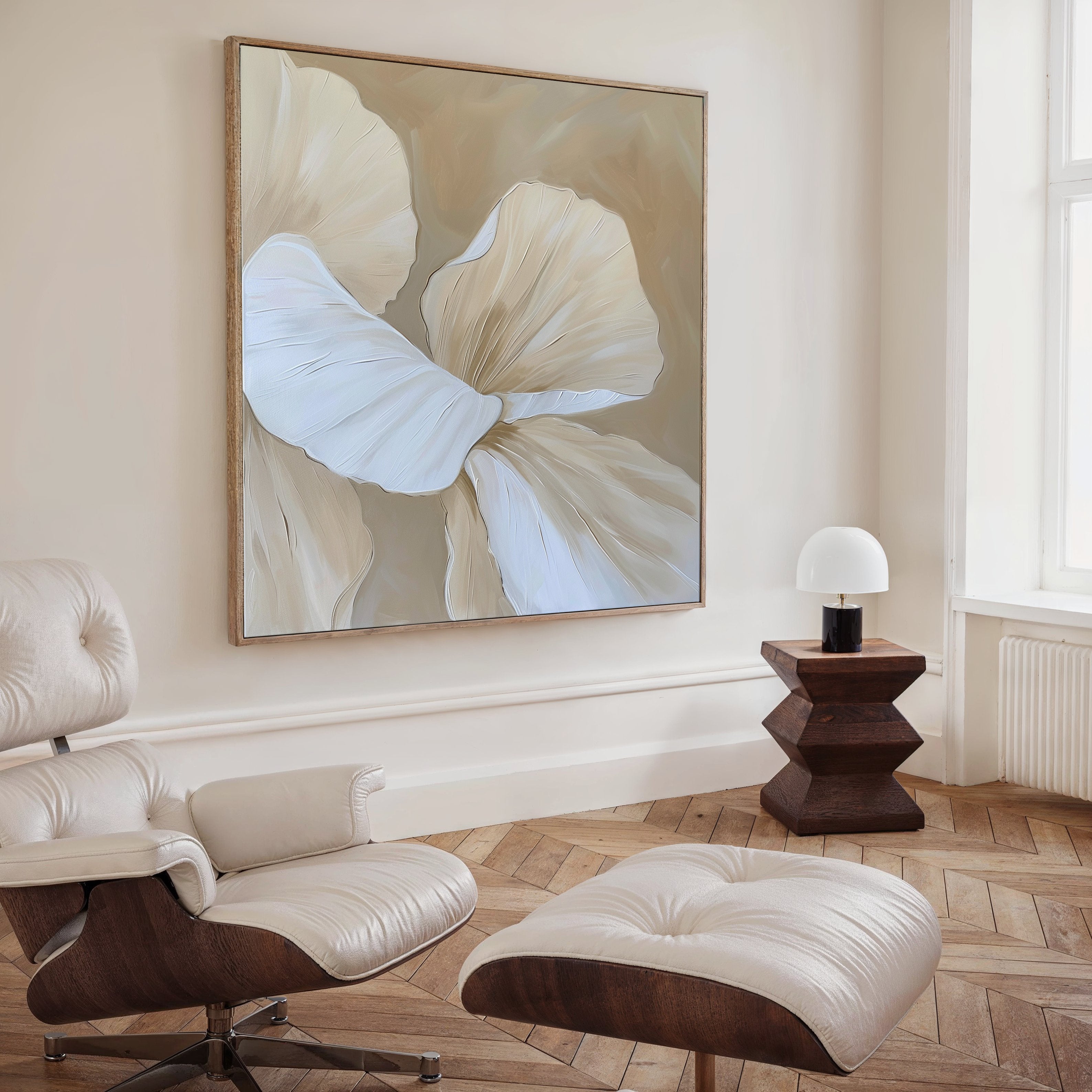 A modern living room featuring a cream leather lounge chair and ottoman, a geometric dark wood side table with a white lamp, and the Floral Whisper Abstract Canvas Art in neutral tones as striking wall décor.