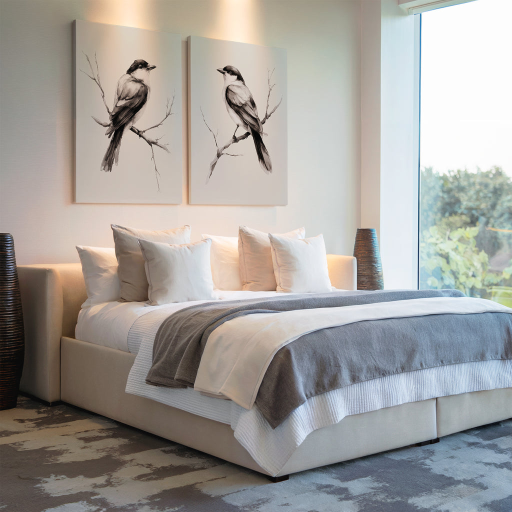 A modern bedroom with a large bed, white and gray bedding, two Still Perch Set of 2 bird art prints above the headboard, and large windows filling the space with natural light.