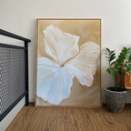 The Aqua Flora Abstract Canvas Art, featuring a soft white flower with beige accents, leans against a light wall on a wooden floor—perfect minimalist decor for your living room near a green plant and black metal railing.