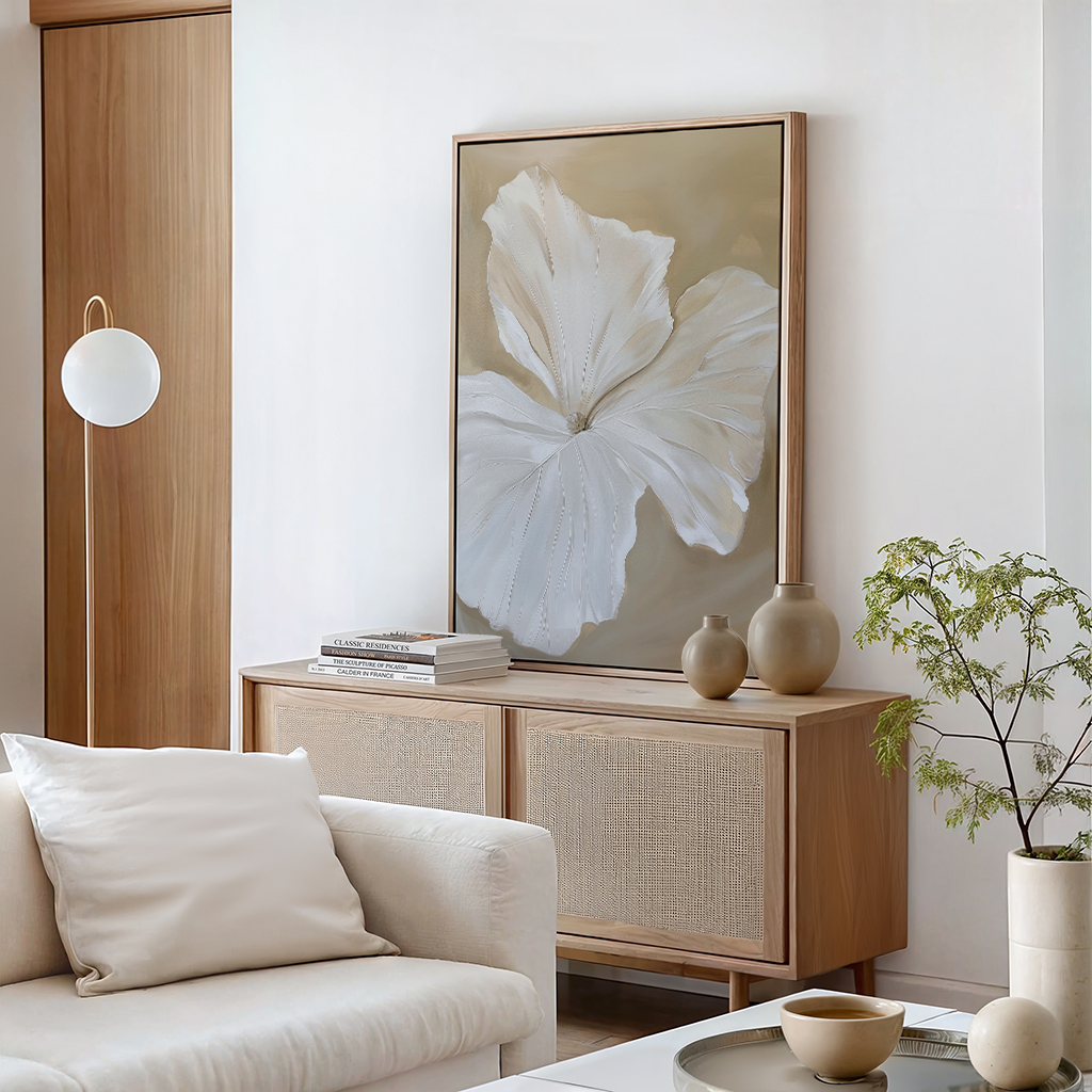 A modern living room features a beige sofa, wooden sideboard, vases, books, a potted plant, and minimalistic earthy decor highlighted by the Aqua Flora Abstract Canvas Art—a large framed painting of a white flower on a neutral background.