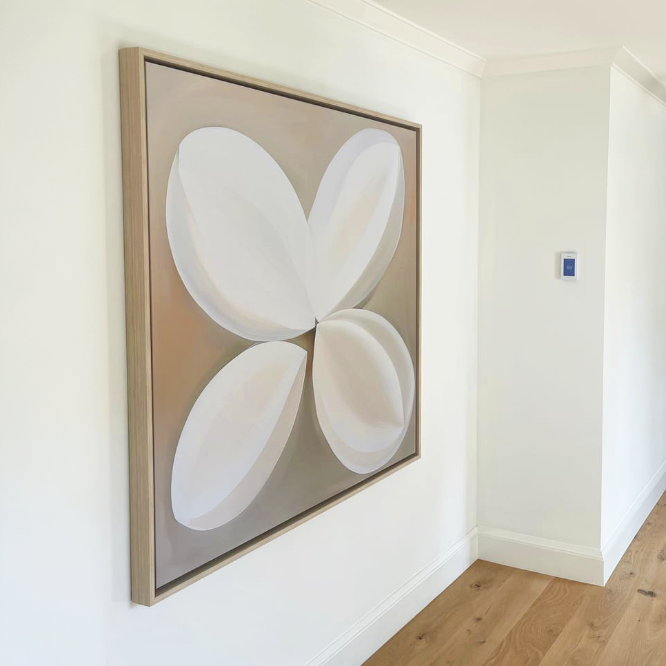 The Clover Harmony Abstract Canvas Art, displaying four overlapping white petal shapes on a beige background, hangs on a white hallway wall with light wood floors and a nearby thermostat.