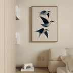 The Abstract Birds in Motion Canvas Art, with blue and beige tones, hangs above a light couch in a minimalist room, creating a serene Nordic Park vibe alongside shelves displaying books and a small white decorative object.