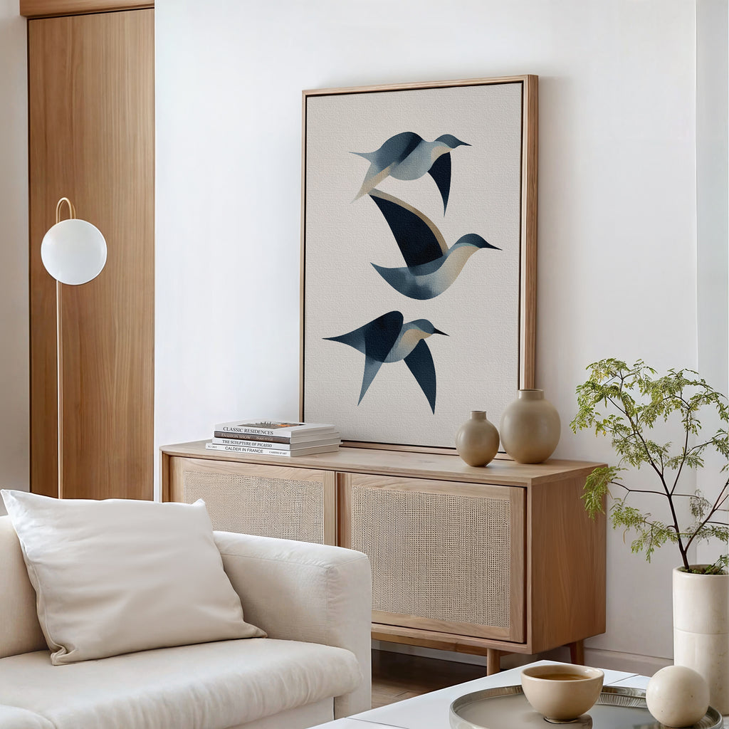 A minimalist living room with a light wood sideboard, Abstract Birds in Motion Canvas Art, neutral ceramics, a white sofa, round coffee table, and small green plant creates a calming Nordic Park-inspired retreat.