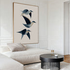 A modern living room with a white sectional sofa, beige cushions, a round black coffee table, and the Abstract Birds in Motion Canvas Art. White paneled walls and minimalist décor evoke a serene Nordic Park-inspired atmosphere.